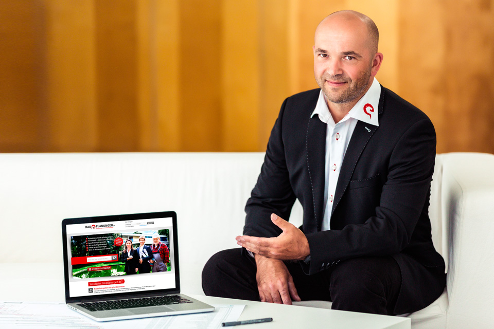 Darstellung von Herrn Köhler auf einer Coach mit einem Laptop, der die Webseite von Bauplanungen.de zeigt.